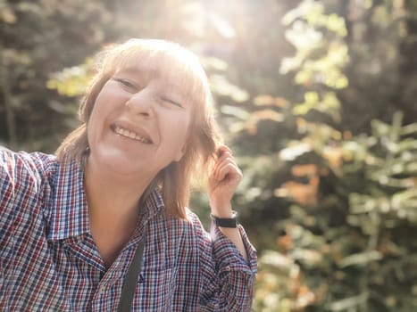 Blonde woman smiles brightly during her autumn adventure in a beautiful forest, capturing the moment in a joyful selfie.