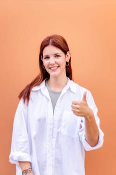 young woman giving a thumb up gesture while smiling looking at camera in a positive and friendly mood suggesting that she is happy and content, copyspace for text