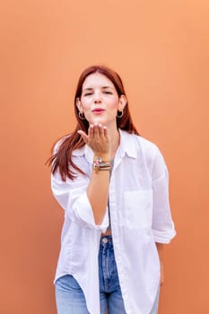 young woman giving a kiss with hand while smiling looking at camera in a positive and friendly mood, concept of love, copyspace for text