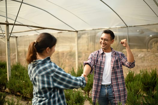 Happy farmers celebrating a successful business deal with handshake inside a greenhouse.