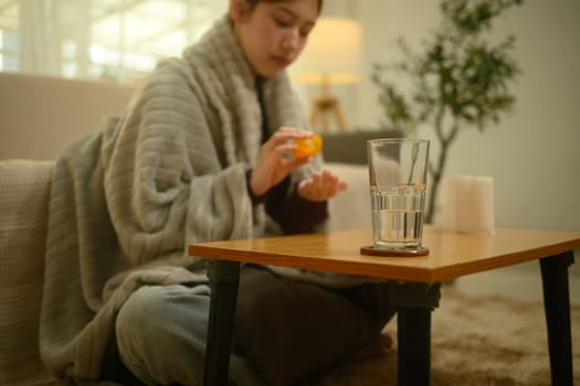 A glass of water on a wooden table with sick woman taking pill in background.