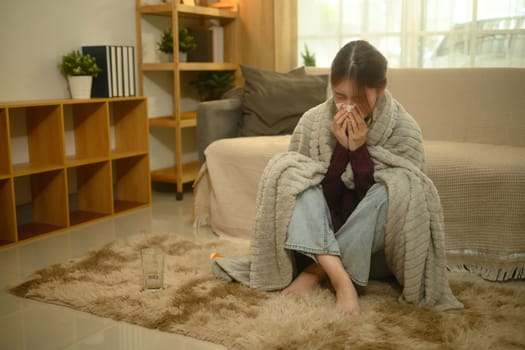 Young woman suffering from a cold or flu, sneezing while wrapped in a blanket.
