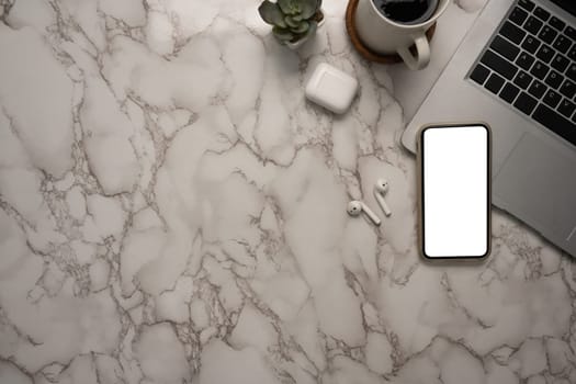Stylish marble desk with laptop, smartphone, wireless earbuds and a coffee cup.
