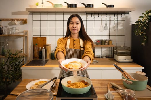 Happy woman presents a delicious plate of spicy noodles topped with fried egg.