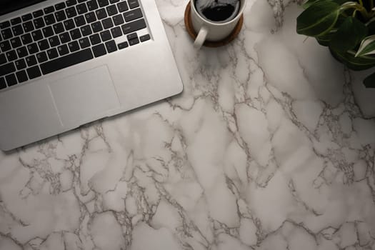 top-view of a stylish marble desk featuring a sleek laptop, a cup of black coffee, and a potted plant..