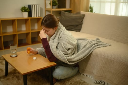 Sick young woman wrapped in a warm blanket and taking medicine for recovery.