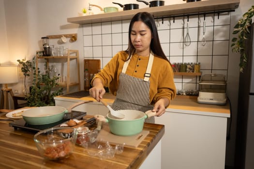 Young Asian woman wearing apron preparing meal in a warm kitchen.