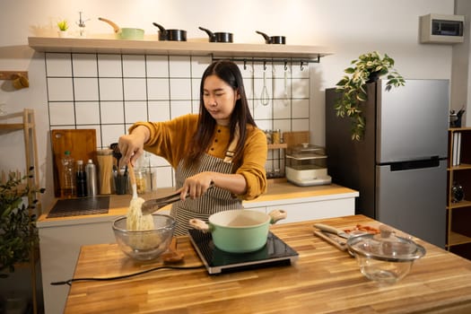 Young asian woman in an apron cooking a simple meal in her home kitchen.