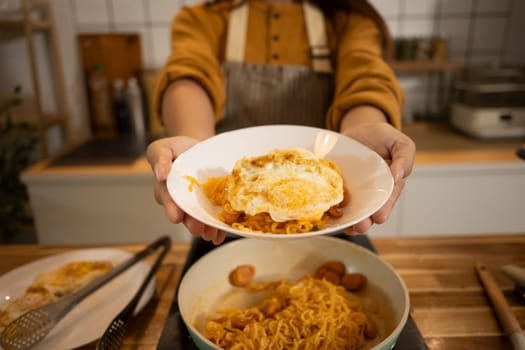 Close up of woman holding a plate of spicy noodles topped with a fried egg.