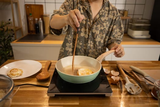 Young man preparing breakfast, frying eggs in a ceramic pan.