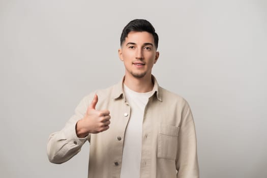 Reliable and satisfied customer endorsement as a handsome caucasian man in his 30s gives a thumbs-up with a neutral smile, approving a product or service.