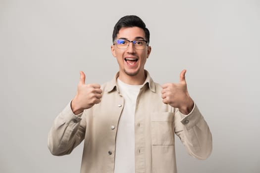 Man inspiring confidence in a product or service shows double thumbs-up with a wide smile. Wearing eyeglasses and beige clothes, he poses naturally with a candid and approachable vibe.