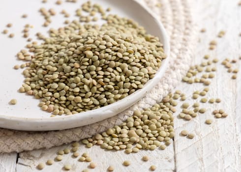 Plate full of dried raw green lentils on white table close up. Healthy raw vegetarian food, legumes plant-based protein source. Traditional mediterranean cousin ingredient