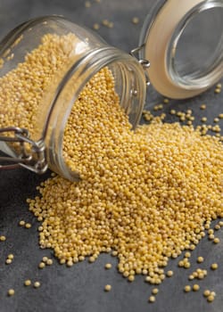 Glass jar of raw yellow pearl hulled millet grain on gray table closeup. Ancient uncooked pseudocereal seeds. Organic healthy superfood. Gluten free alternative seeds