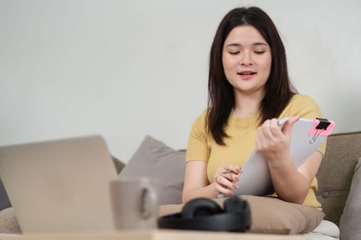 A woman working from home actively participates in a video call, analyzing notes and preparing to discuss her ideas. The image captures the essence of remote teamwork and communication.