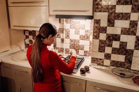 Woman in red uses a kitchen stove. Brown-haired, ponytail. Back view. Checkered backsplash. Cooking.