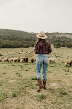 A woman wearing a hat and boots walks through a field of sheep. The scene is peaceful and serene, with the woman and the sheep coexisting in harmony