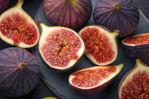 Fresh figs are displayed on a dark slate platter. Whole and sliced figs reveal vibrant, juicy interiors. The warm tones highlight the fruits natural beauty and freshness.