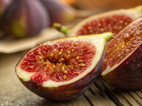 Figs are freshly cut to showcase their vibrant red interior filled with tiny seeds. The rustic wooden surface adds a warm, natural ambiance to the presentation, highlighting the fruits freshness.