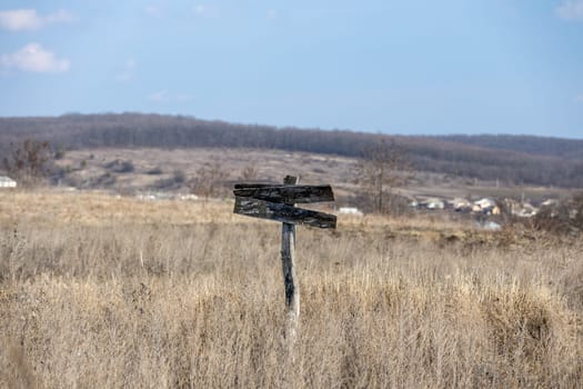 Old weathered wooden sign with empty planks pointing in opposite directions in dry grass field, suggesting a difficult choice or uncertainty