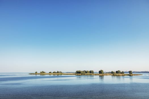 Beautiful landscape showing small islands reflecting on the calm water of a river under a clear blue sky