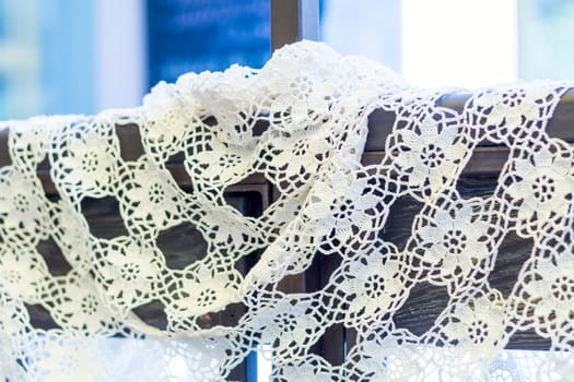 Delicate white crochet lace draped over a wooden frame, adding a touch of vintage charm and elegance to the scene