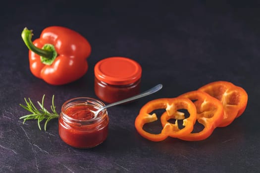 Jars of delicious homemade sauce with fresh red bell peppers and rosemary, creating a vibrant culinary scene