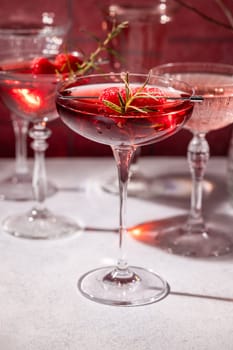 Coupe glasses filled with vibrant red cocktails, adorned with fresh raspberries and a fragrant rosemary sprig, create a sophisticated and festive atmosphere