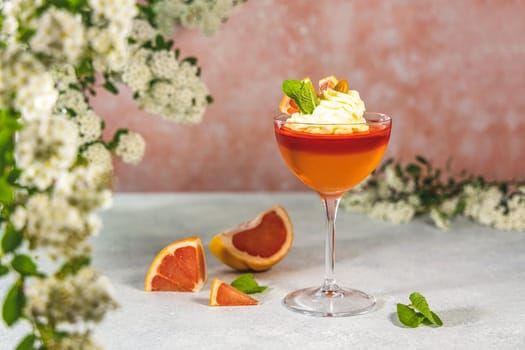 Grapefruit jelly dessert garnished with whipped cream, mint, and grapefruit slices, creating a refreshing and visually appealing treat
