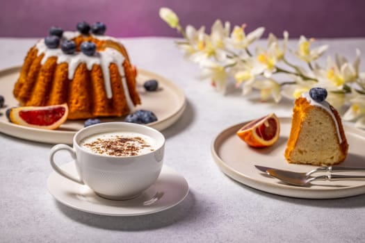 Enjoying a slice of gugelhupf with blueberries and blood orange alongside a cappuccino, creating a delightful breakfast scene