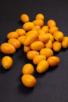 Fresh kumquats scattered across a dark surface, showcasing a vibrant contrast of colors and textures, highlighting their juicy, sweet, and sour appeal