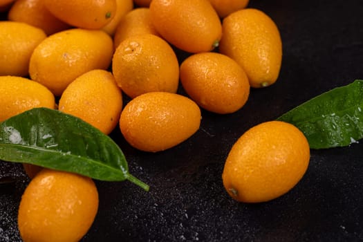 Vibrant kumquats, adorned with water droplets, create a colorful contrast against a dark backdrop, accompanied by fresh green leaves