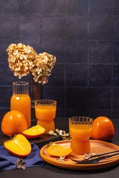 Persimmon juice served in elegant glasses with fresh and ripe persimmon fruits, accompanied by dried flowers, creating a cozy autumn atmosphere