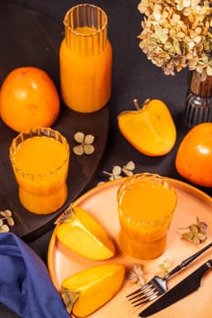 Two glasses and a carafe of persimmon juice are surrounded by fresh fruits and dried flowers, creating a vibrant and autumnal scene