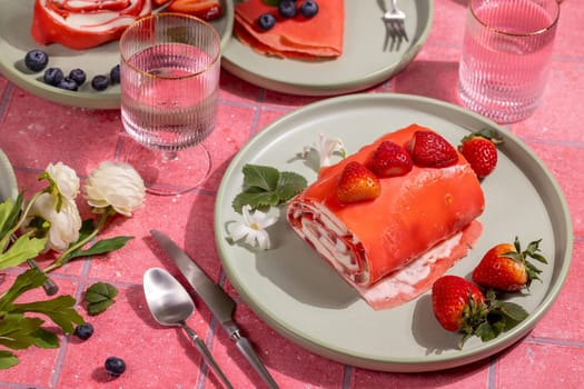 Strawberry crepe roll cake with cream and fresh strawberries served on a plate on a pink table, ready to enjoy