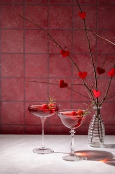 Two raspberry and rosemary cocktails are garnished and ready for a romantic valentine's day celebration