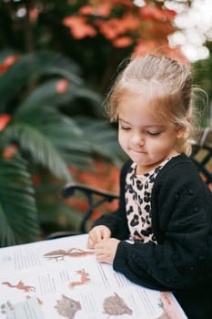 Little girl thoughtfully reads a book of fairy tales while sitting on a bench in the autumn garden. High quality photo