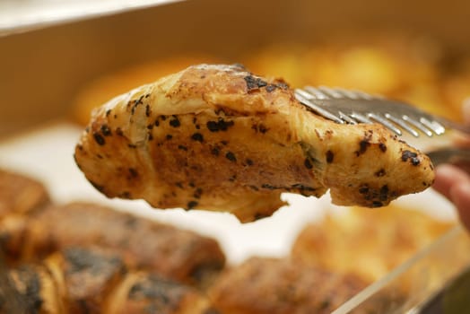 A hand serves a grilled chicken breast at a buffet setup, showcasing food.