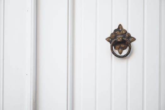 An elegant brass door knocker adorns a white wooden surface.
