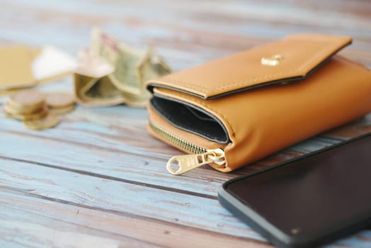 A brown wallet rests on a wooden surface with coins and cash nearby.