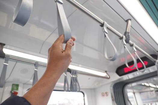 A commuter stands in an urban train, gripping a safety strap while riding.
