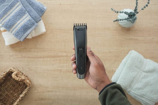A person uses a hair clipper amidst clean towels and decor in the bathroom.