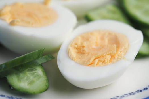 Sliced hard-boiled eggs are arranged on a plate with cucumber.