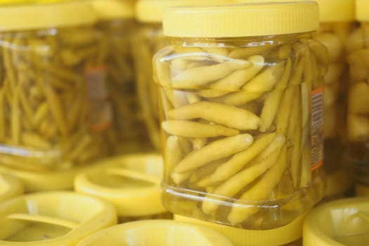 Jars filled with yellow pickled peppers are arranged for sale in a market.