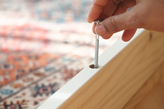 Hand inserting a screw into a wooden frame during assembly.