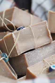 Artisan soap bars are stacked with decorative beads and twine in a market.