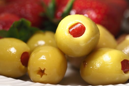 Delicious green olives filled with red pimento on a white plate.