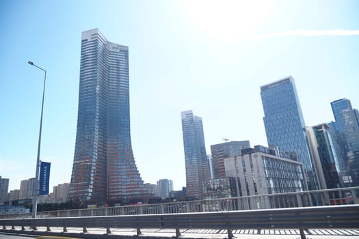 Tall buildings reach skyward beside a busy roadway on a sunny day.