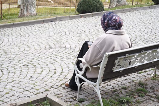 Elderly woman with a headscarf enjoys a peaceful moment in a park.