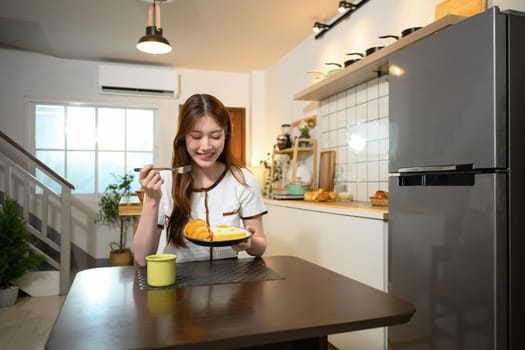 Beautiful young woman enjoying a delicious breakfast in a cozy home kitchen.